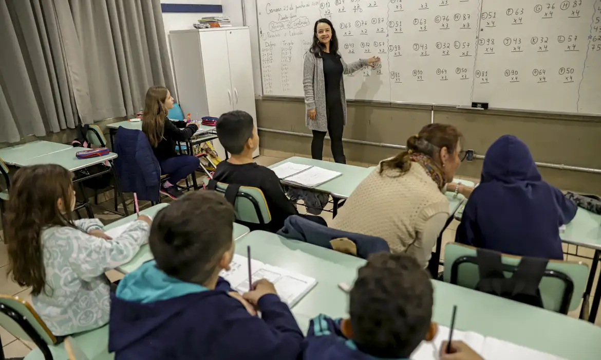 a woman standing in front of a whiteboard with students in the background