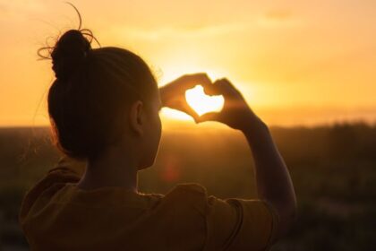 mulher fazendo coração com as mãos em torno do sol