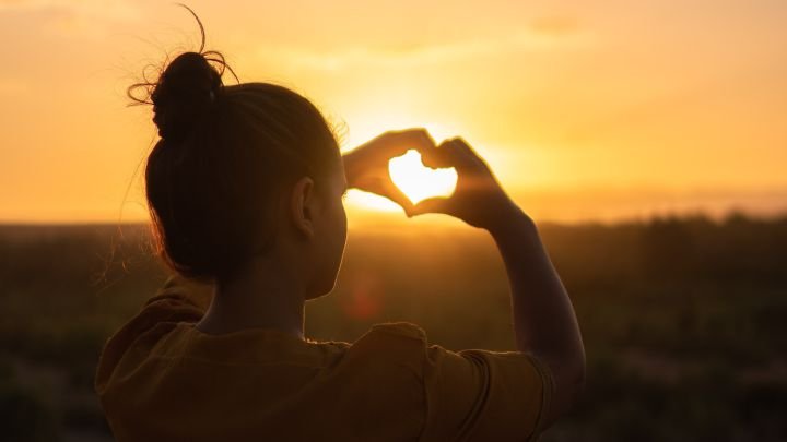 mulher fazendo coração com as mãos em torno do sol